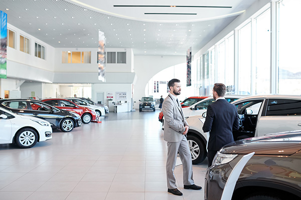 two men discussing cars in a modern showroom with several vehicles displayed inside