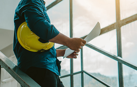 man in blue shirt holding plans with yellow safety helmet on stairs showcasing construction site details and project management for six key elements