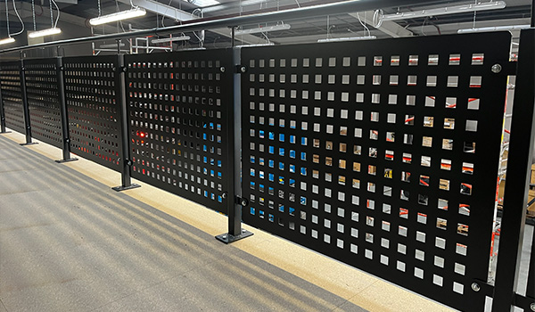 black metal fence with square perforations creating a pattern in an indoor setting featuring seven sections of design